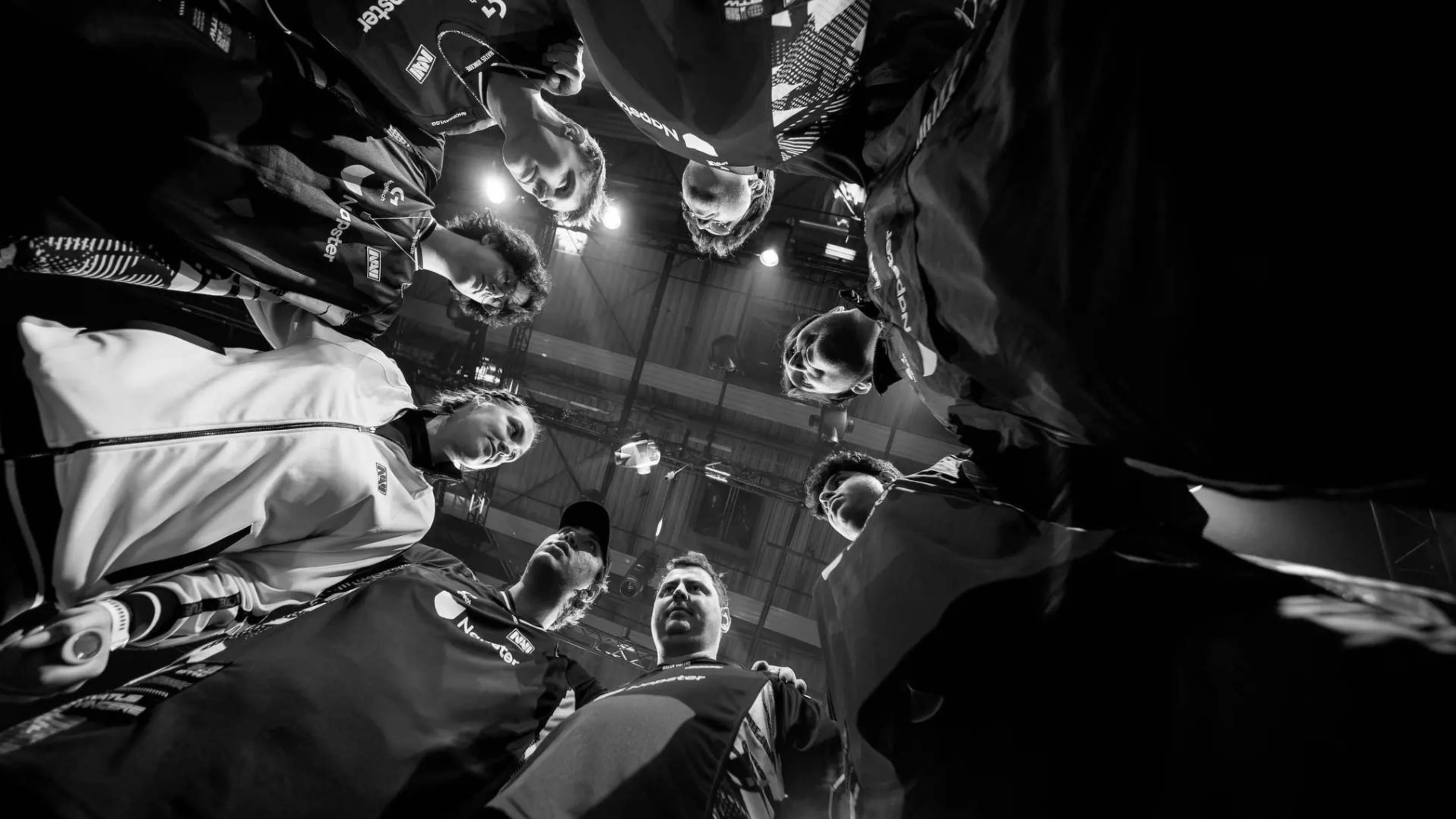 NAVI VALORANT team members gather in a close huddle beneath arena lights in a black-and-white photograph.