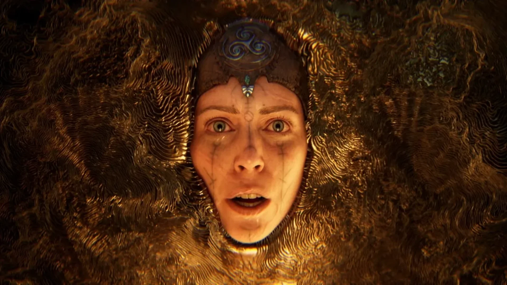 Senua's face emerges from a dark golden organic surface in artwork from Ninja Theory's upcoming game.