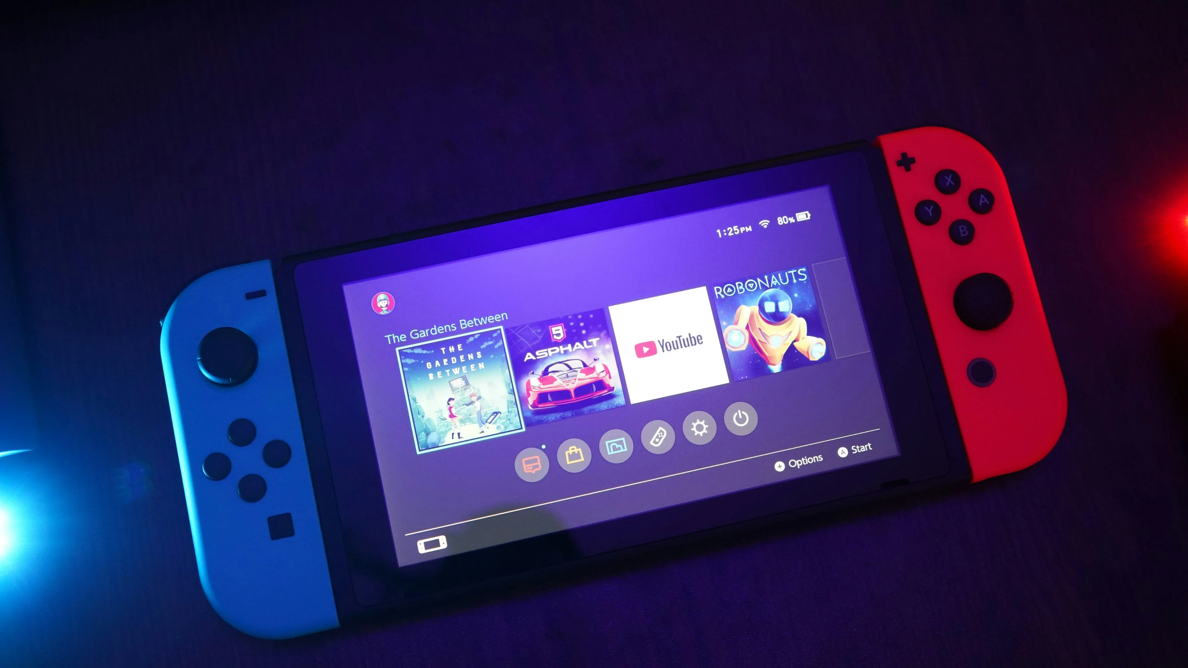 Original Nintendo Switch console with blue and red Joy-Con controllers displays its home menu against a dark purple background.