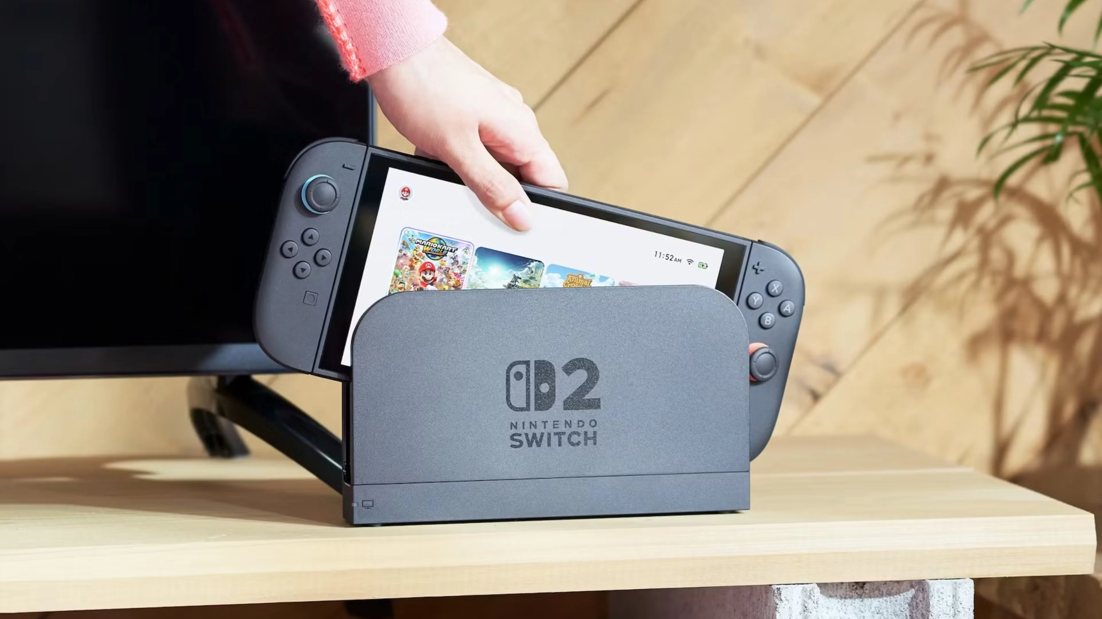 A hand places a Nintendo Switch 2 handheld into its docking station, with the console's home screen visible.