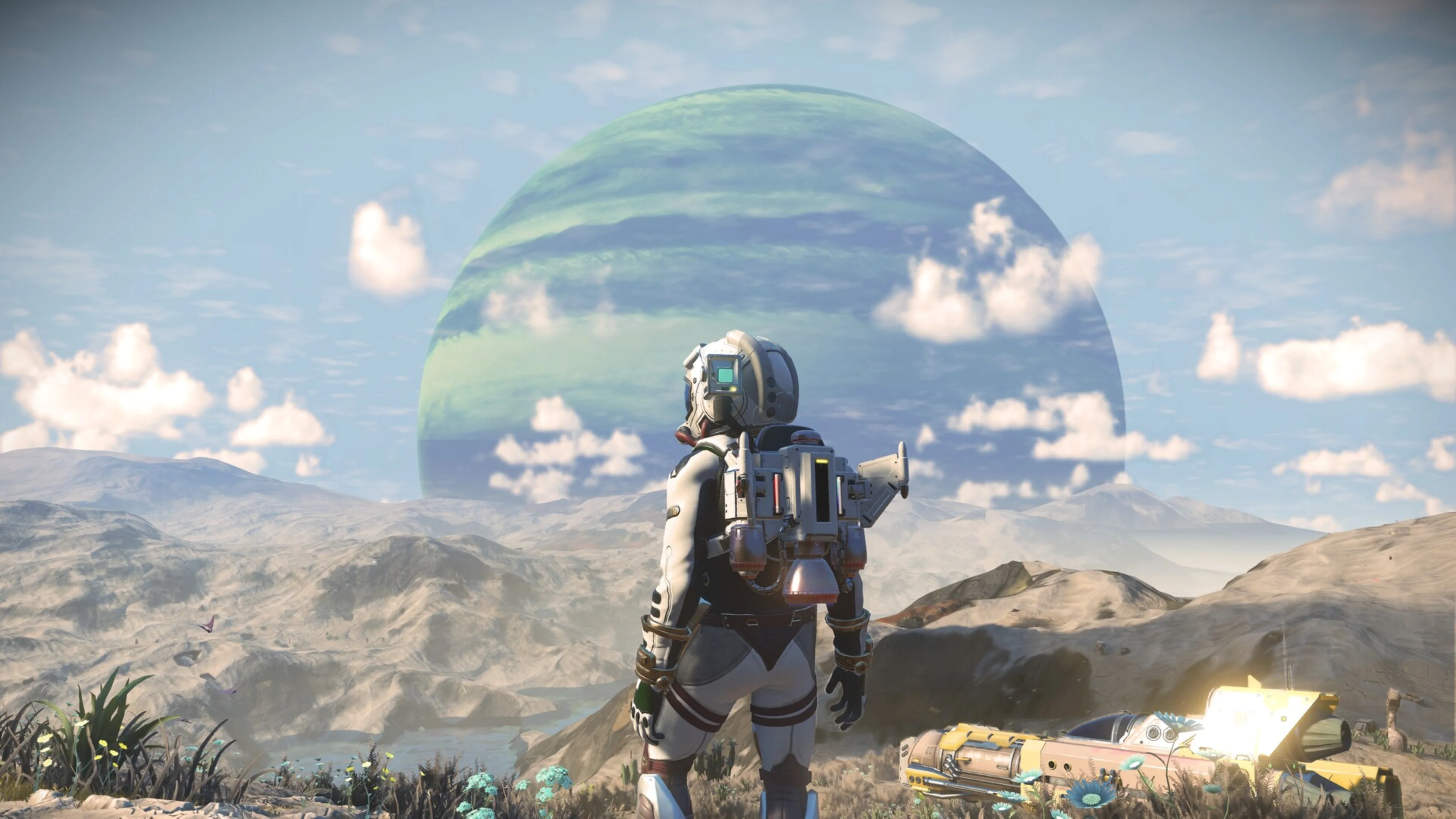 A No Man's Sky explorer in a spacesuit stands on a rocky landscape facing a huge green planet beneath a bright sky.