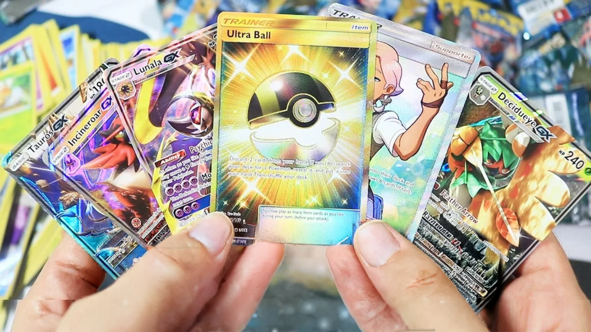 A person holds several Pokémon TCG cards including Lunala GX, Decidueye GX and a gold Ultra Ball Trainer card.