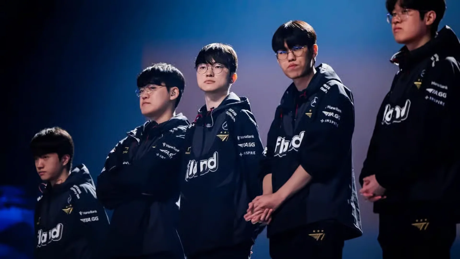 T1 League of Legends players stand together on stage wearing black team jackets.