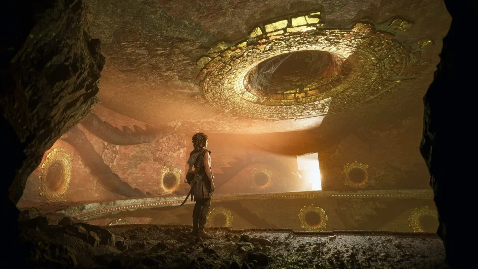 Sophia stands inside underground ruins surrounded by large golden circular structures in Resonance: A Plague Tale Legacy
