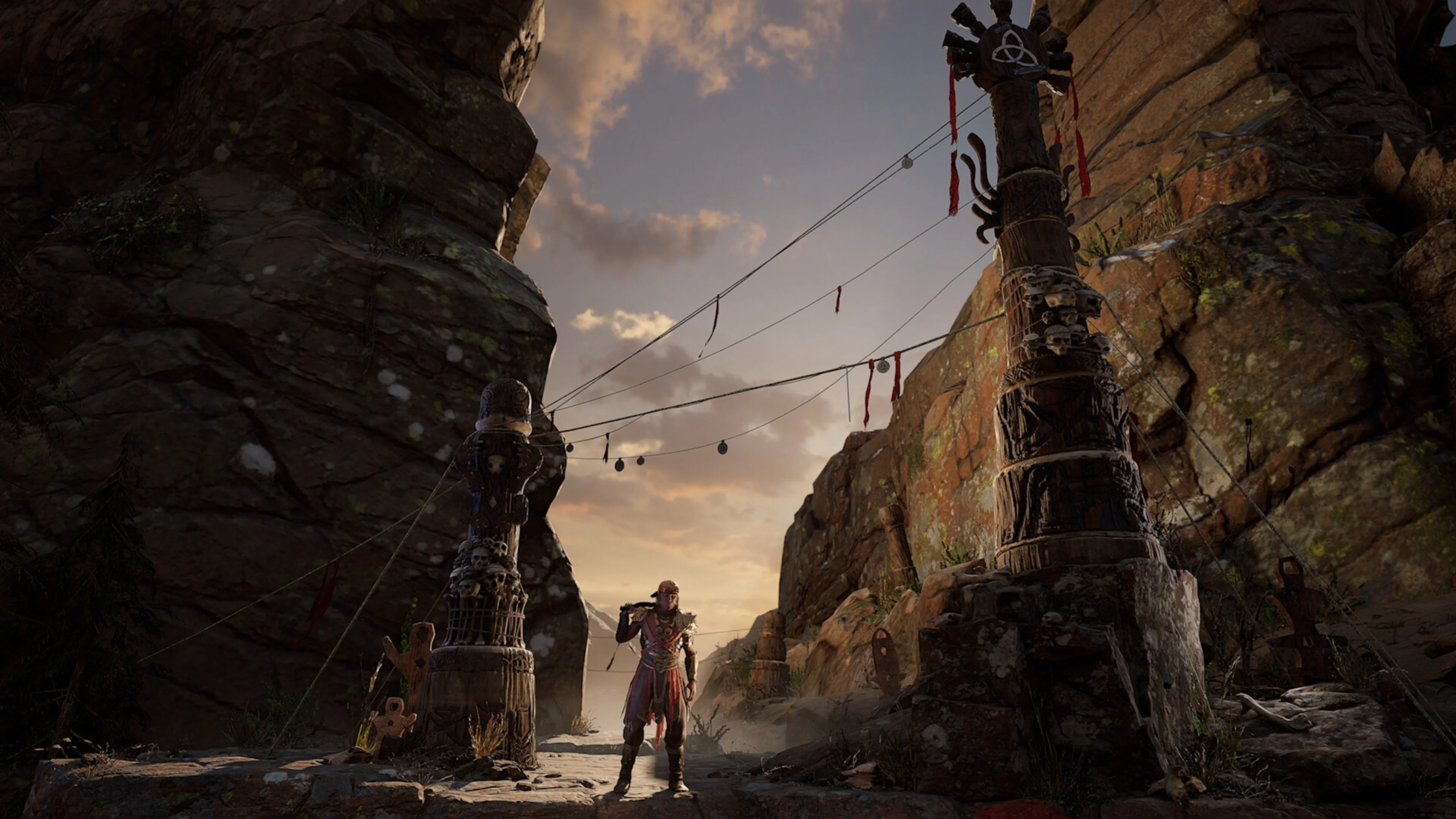 An adventurer stands between rocky canyon walls and wooden ritual totems decorated with skulls and hanging ornaments in Rewolt.