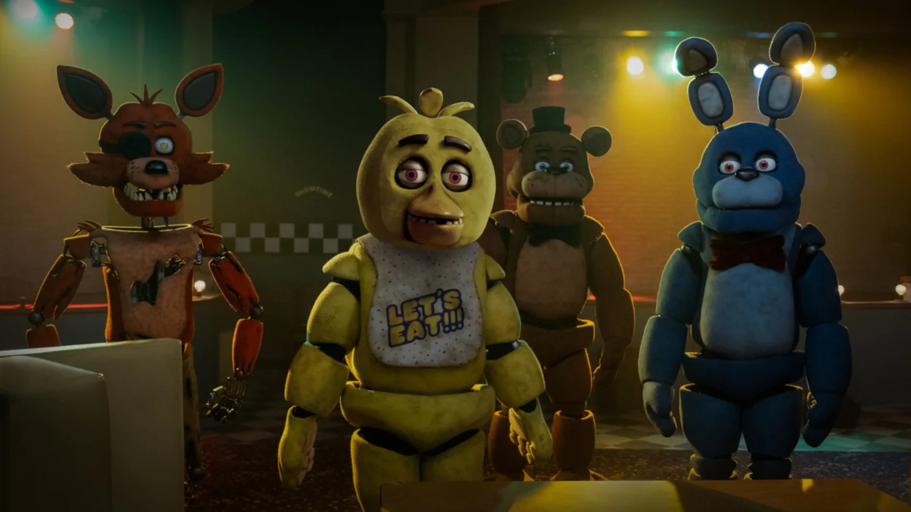 Freddy Fazbear, Bonnie, Chica and Foxy standing together inside a dimly lit room with colorful overhead lights.