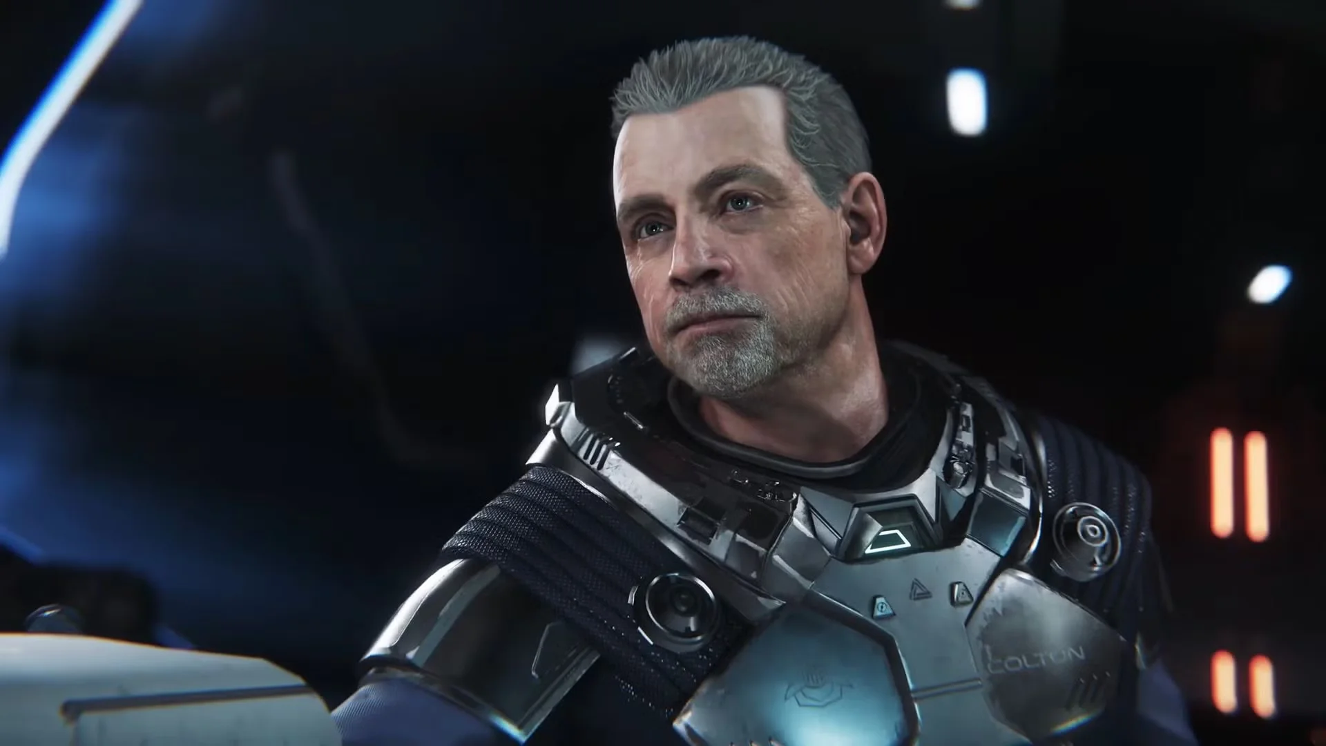 A gray-haired man with a trimmed beard wears futuristic silver armor inside a dimly lit spacecraft in Squadron 42.