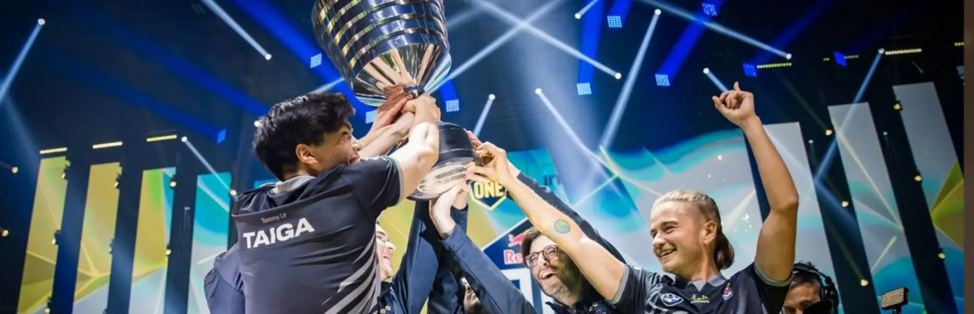 Team OG celebrating with a trophy after winning an esports tournament on stage.