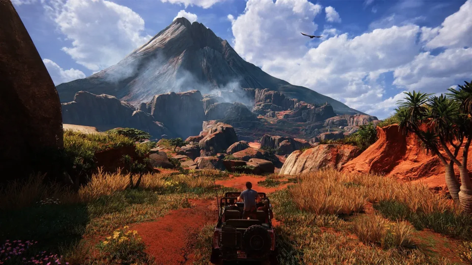 Nathan Drake drives a jeep through a red dirt landscape toward a towering mountain in Uncharted 4.