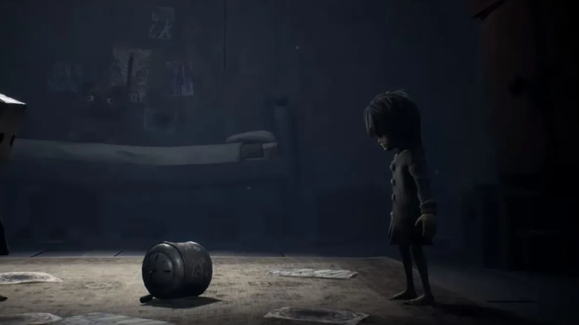 Mono stands beside a cylindrical object in a dimly lit room in Little Nightmares II.