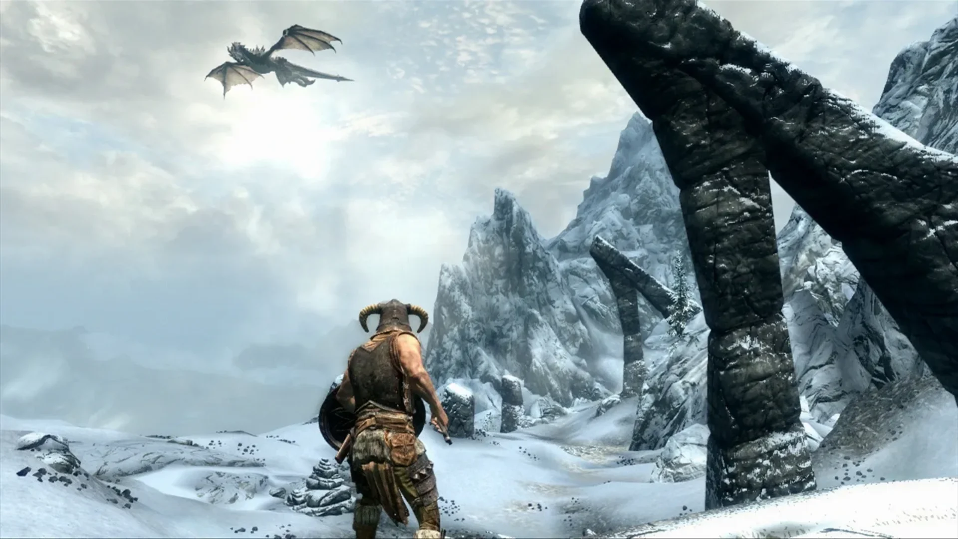The Dragonborn watches a dragon fly above snowy mountain ruins in The Elder Scrolls V: Skyrim.