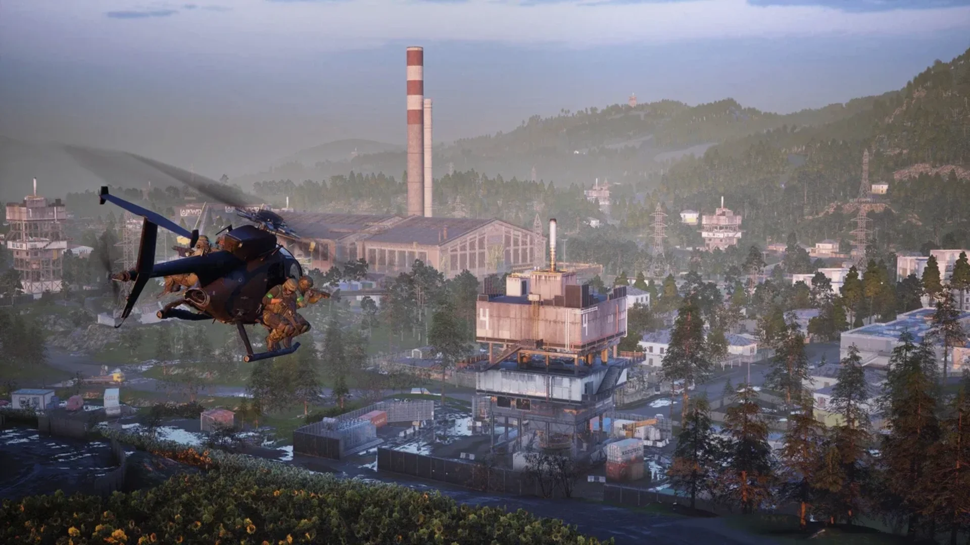 A WARDOGS helicopter carries soldiers above an industrial complex surrounded by forest and mountains.