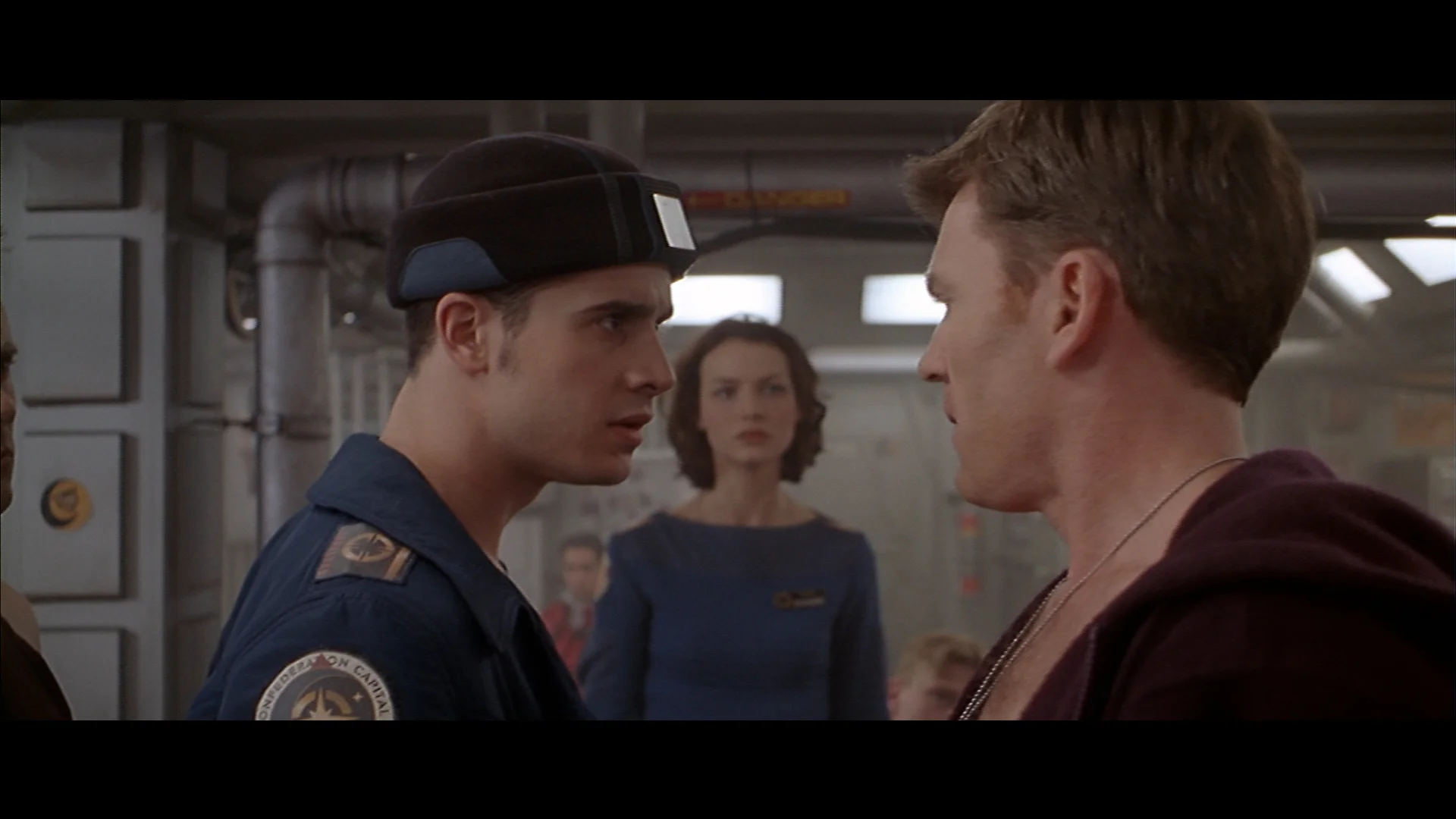 Two men face each other aboard a spacecraft while a woman watches from behind in a Wing Commander III live-action scene.