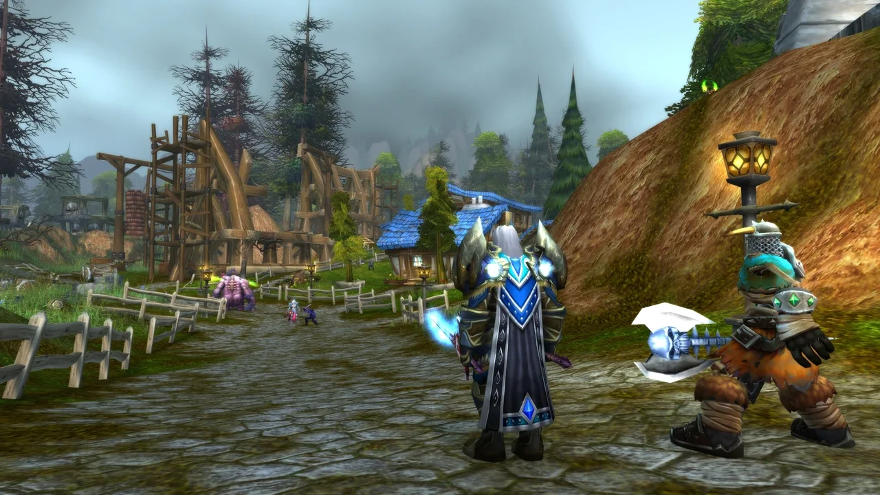 World of Warcraft character standing on a village road beside an NPC, with wooden buildings and trees in the background.