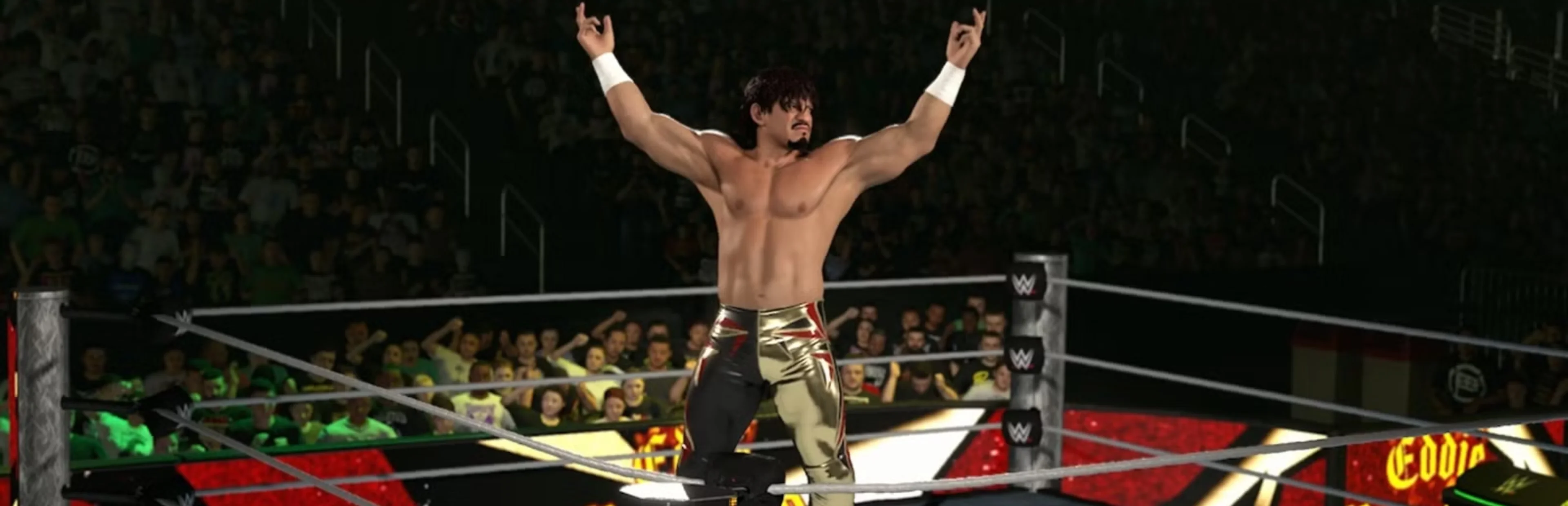 A male wrestler raises both arms inside a WWE 2K26 wrestling ring as fans watch from the arena stands.