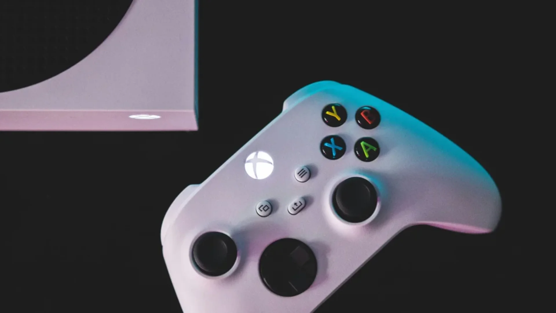 A white Xbox wireless controller sits beside part of an Xbox Series console against a dark background.