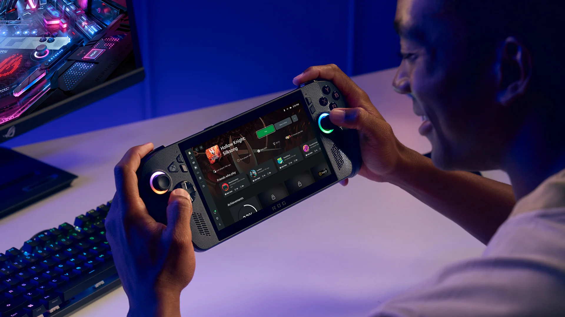 Player holds an Xbox gaming handheld displaying the Xbox interface while sitting at a gaming setup.