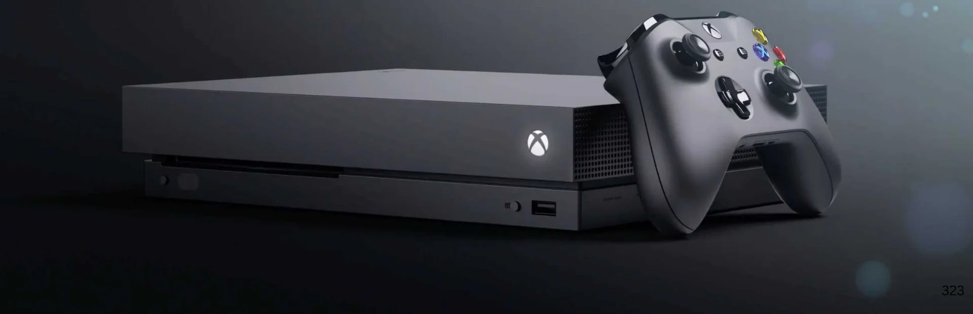 Alt Text: Black Xbox One X console rests horizontally with a matching Xbox wireless controller leaning against its right side.
